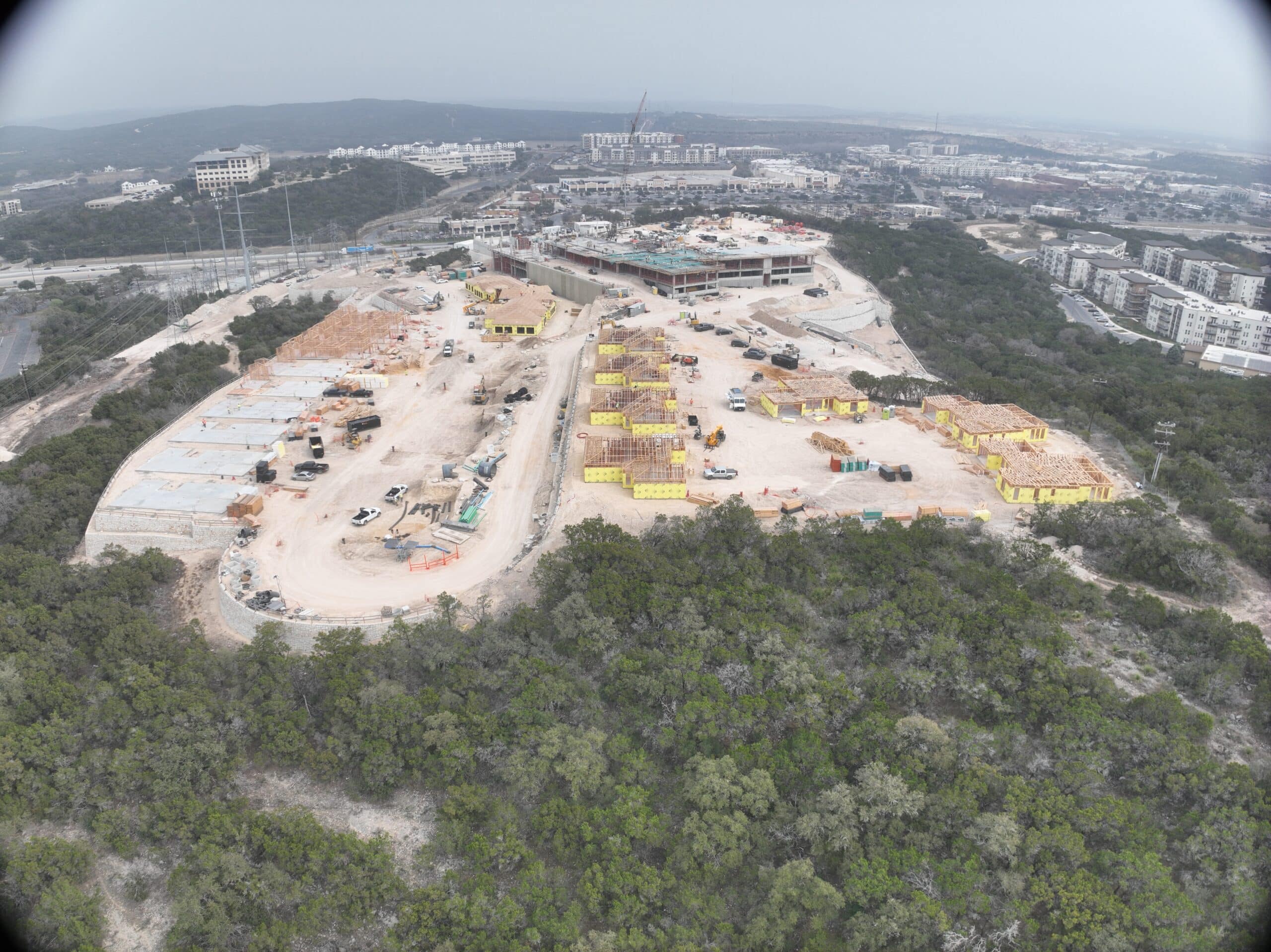 Bella Vida construction site with crews working on site walls, utilities, concrete slabs, and new framing at the Memory Care building, Phase 3 villas, and quadplex foundations.