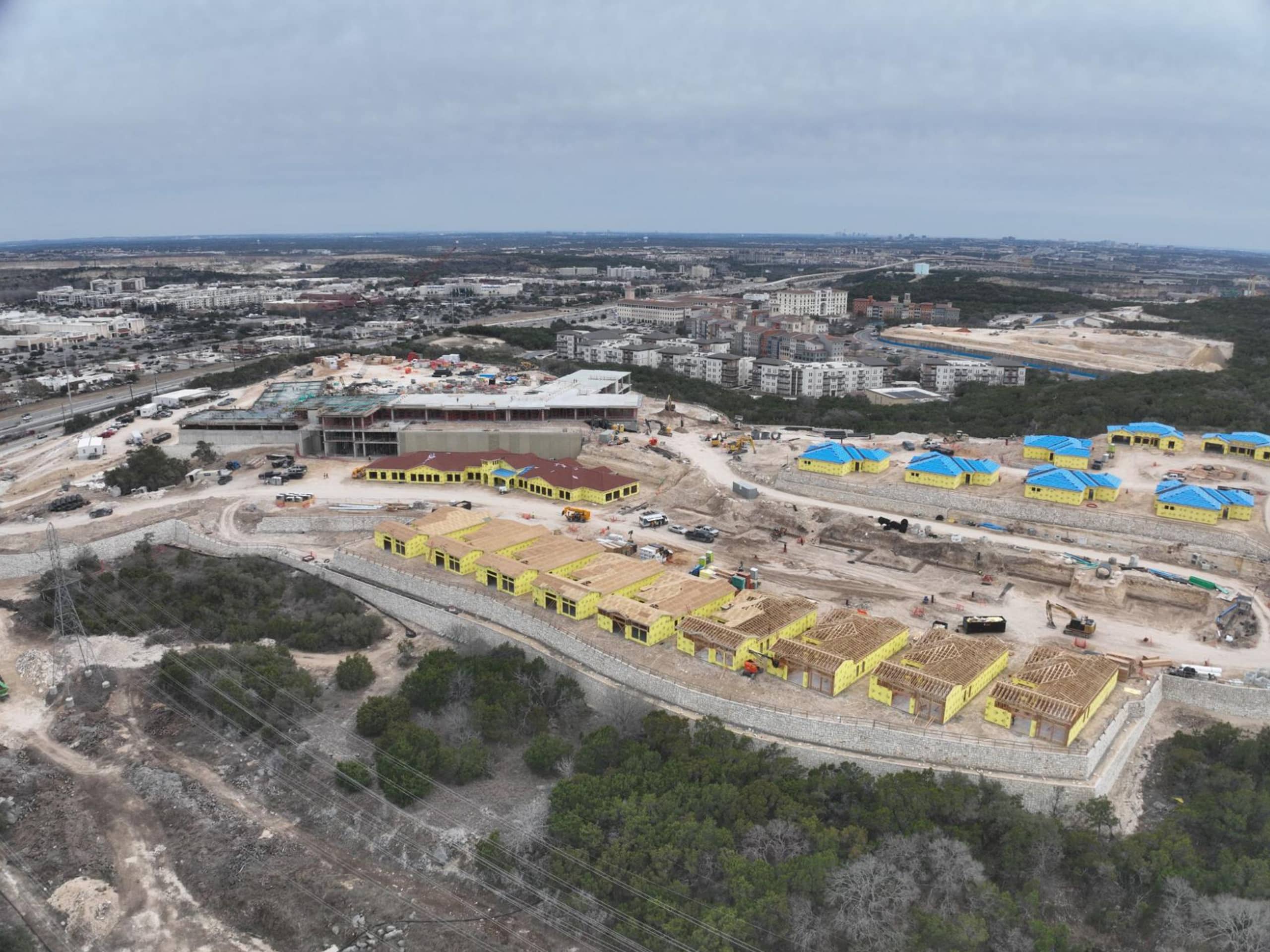 Bella Vida construction site with crews working on site walls, utilities, concrete slabs, and new framing at the Memory Care building, Phase 3 villas, and quadplex foundations.