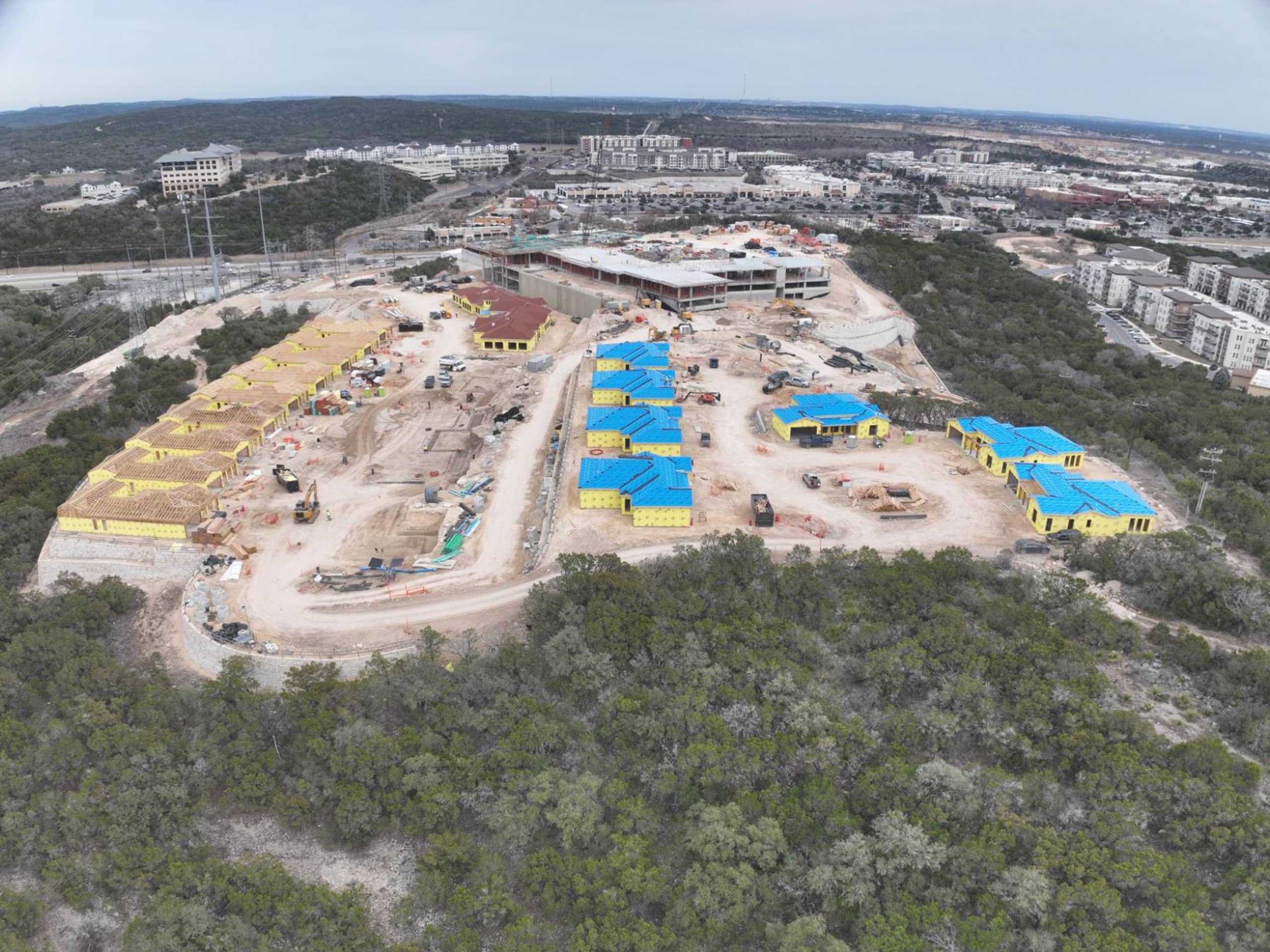 Bella Vida construction site with crews working on site walls, utilities, concrete slabs, and new framing at the Memory Care building, Phase 3 villas, and quadplex foundations.