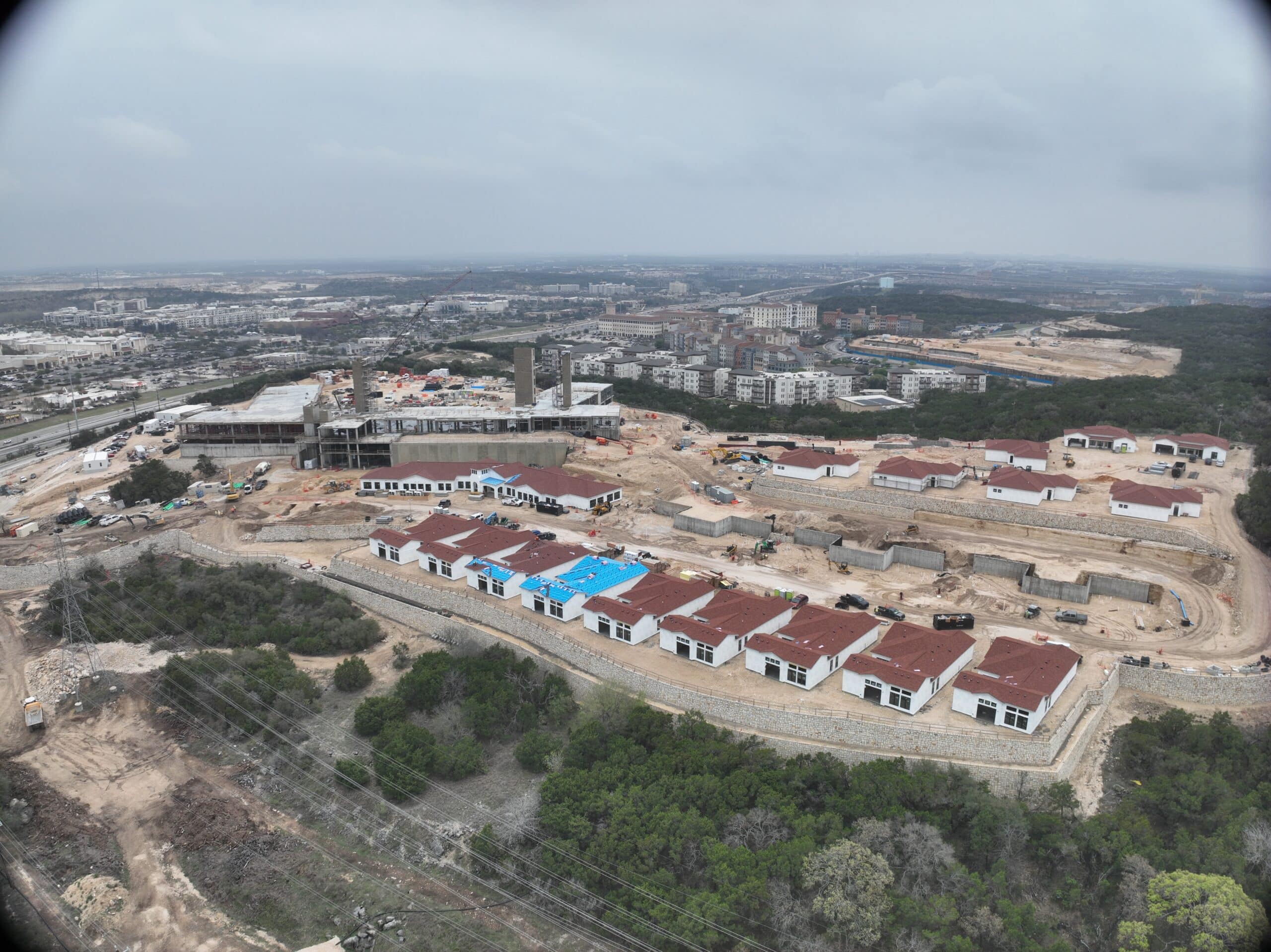 Bella Vida construction site with crews working on site walls, utilities, concrete slabs, and new framing at the Memory Care building, Phase 3 villas, and quadplex foundations.