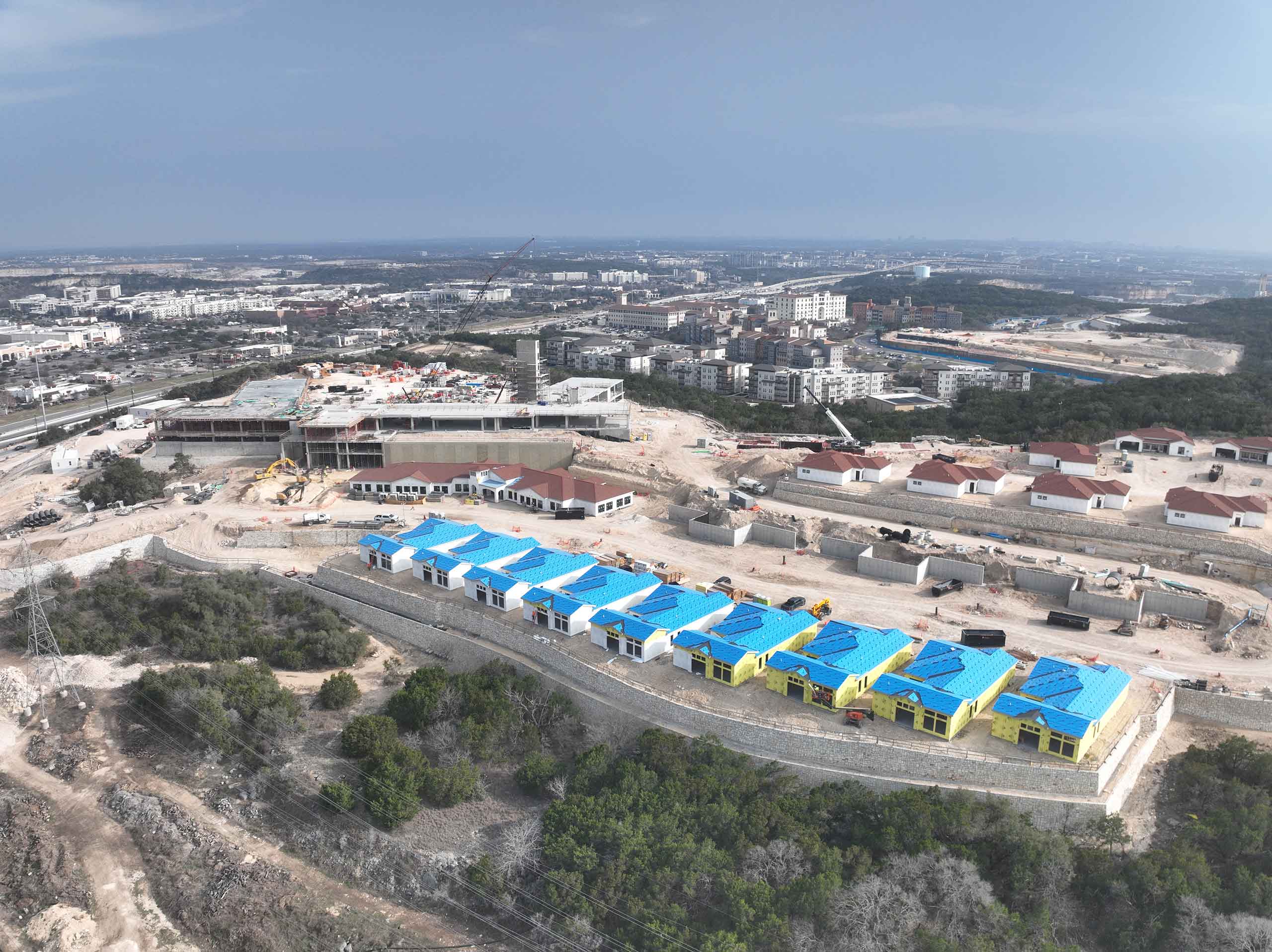 Bella Vida construction site with crews working on site walls, utilities, concrete slabs, and new framing at the Memory Care building, Phase 3 villas, and quadplex foundations.