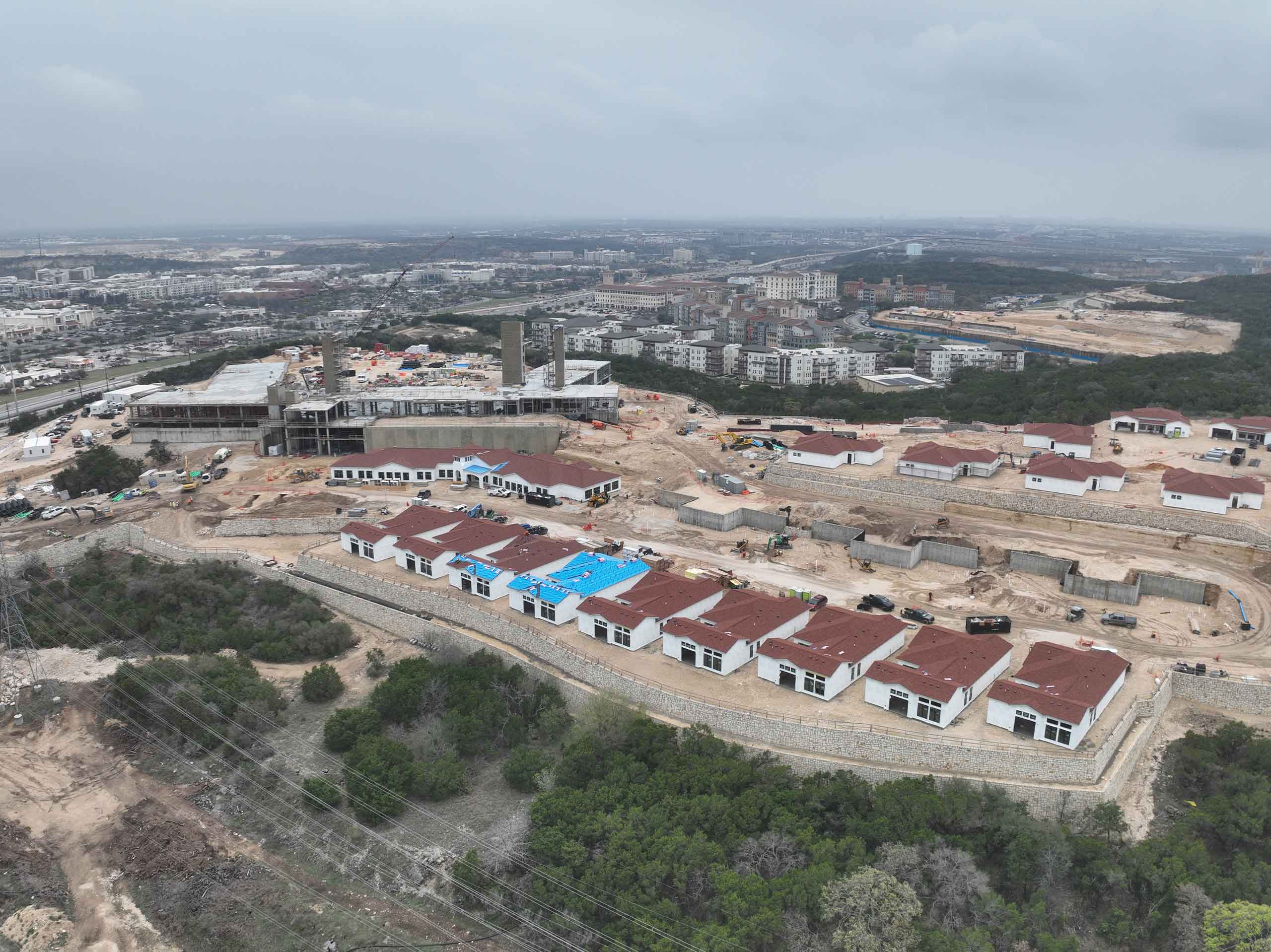 Bella Vida construction site with crews working on site walls, utilities, concrete slabs, and new framing at the Memory Care building, Phase 3 villas, and quadplex foundations.